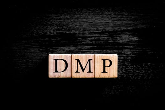 Acronym DMP- debt management plan. Wooden small cubes with letters isolated on black background with copy space available. Business Concept image.