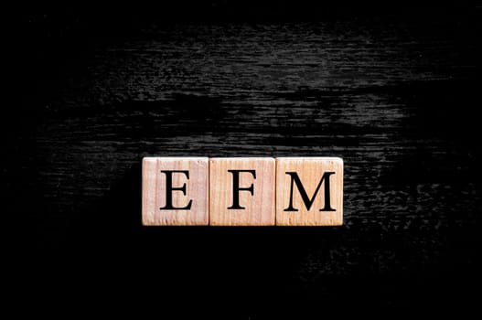 Acronym EFM - enterprise feedback management. Wooden small cubes with letters isolated on black background with copy space available. Business Concept image.