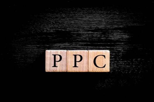 Acronym PPC - Pay per Click. Wooden small cubes with letters isolated on black background with copy space available. Business Concept image.