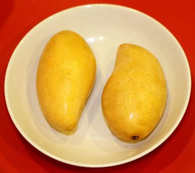 Two yellow delicious mango lie on a plate