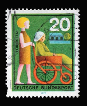 Stamp printed in Germany showing a helper pushes a wheelchair, Volunteer Nursing Aid, circa 1970