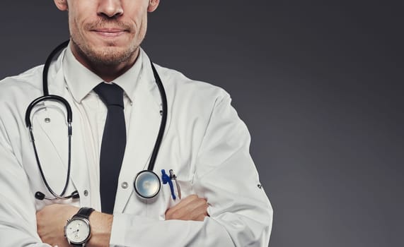 Smiling doctor's midsection with arms crossed, standing against a gray background
