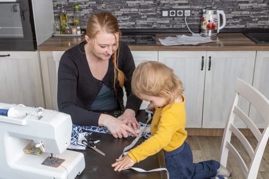 Young mother is sewing with her little son together. Horizontally.