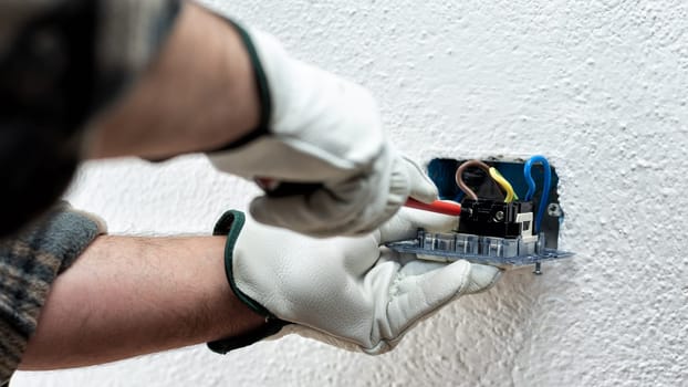 Electrician worker with screwdriver fixes electrical cables in the terminals of the socket of an electrical system. Working safely with protective gloves. Construction industry.