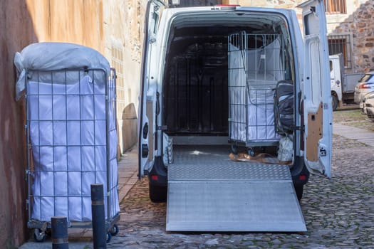 Picking dirt laundry carts. The van equipped with lift ramp is parked in an old town city