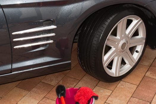Car rims cleaning, car detailing wash concept. Cropped close up photo of male hand in black rubber glove with blue microfiber cloth washing car alloy wheel at car wash service