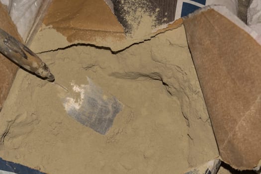 Close-up of plaster trowel in full open paper bag of putty powder for wall decoration,caulk or glaze.Concept of building materials.Finish coating in dry cement powder form.Selective focus,copy space.
