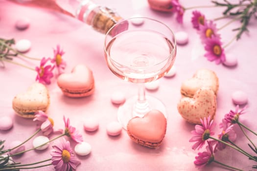 Happy Mothers Day - sweet macarons in heart shape and glass of rose sparkling wine with flowers in pink tone
