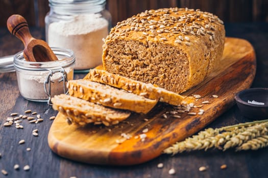 Homemade wholemeal spelt bread with sunflower seeds and baking ingredients on wooden background