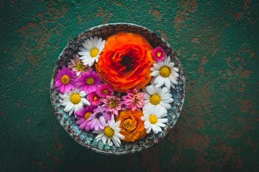 Variation of flowers in bowl on green background with copy space