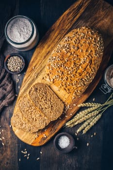 Homemade wholemeal spelt bread with sunflower seeds and baking ingredients on wooden background
