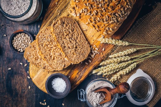 Homemade wholemeal spelt bread with sunflower seeds and baking ingredients on wooden background