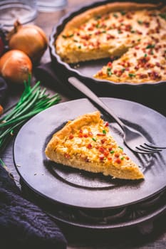 Piece of homemade onion tart or pie with bacon and chive on wooden background