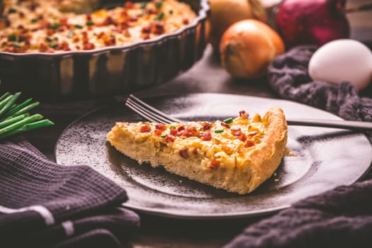 Piece of homemade onion tart or pie with bacon and chive on wooden background