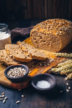 Homemade wholemeal spelt bread with sunflower seeds and baking ingredients on wooden background