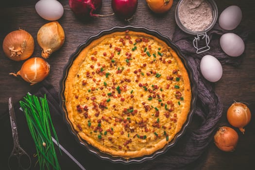 Homemade onion tart or pie with bacon and chives on wooden background