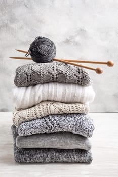 Stack of cozy knitted sweaters and pullovers with knitting needles on wooden background. Autumn and winter concept