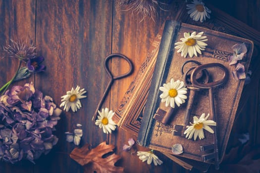 Key to knowledge concept. Old keys on a vintage book with flowers on wooden background.