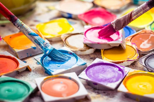 Set of colorful watercolor paints and paintbrushes for painting closeup. Selective focus.