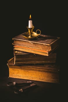 Pile of old antique books with candle and old rusty keys in vintage style on wooden black background