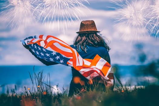 Young happy patriot girl holding the american flag under the 4th of July under fireworks.