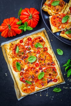 Vegetarian tomato tart or puffed pizza with herbs on black background