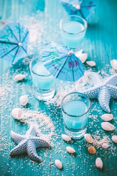 Blue shots for summer with seashells on blue background. Small alcoholic cocktails.