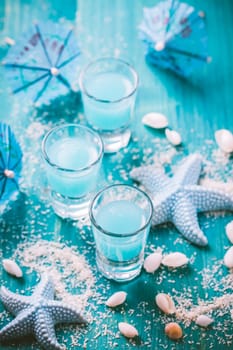 Blue shots for summer with seashells on blue background. Small alcoholic cocktails.