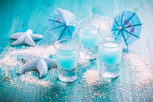 Blue shots for summer with seashells on blue background. Small alcoholic cocktails.