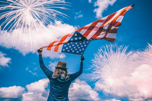 Young happy patriot girl holding the american flag under the 4th of July under fireworks.