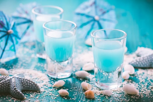 Blue shots for summer with seashells on blue background. Small alcoholic cocktails.