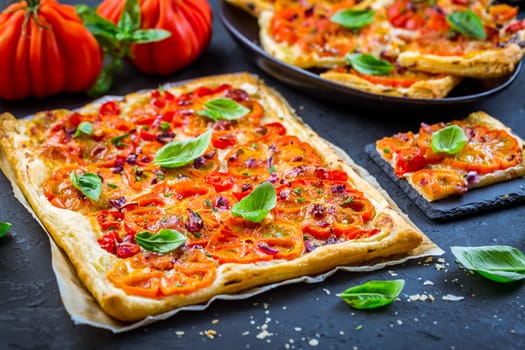 Vegetarian tomato tart or puffed pizza with herbs on black background