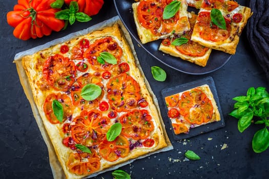Vegetarian tomato tart or puffed pizza with herbs on black background