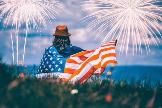 Young happy patriot girl holding the american flag under the 4th of July under fireworks.