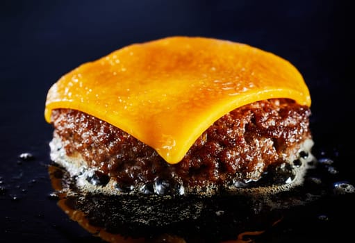 Tasty cheeseburger with beef patty sizzling on a grill in a close up on the melted cheese and juicy meat over a dark background for menu advertising