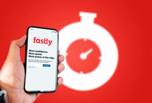 San Francisco, CA, USA, June 2021: A hand holding a phone with the Fastly app on the screen. Red background with blurred Fastly logo. Fastly is an American cloud computing services provider.