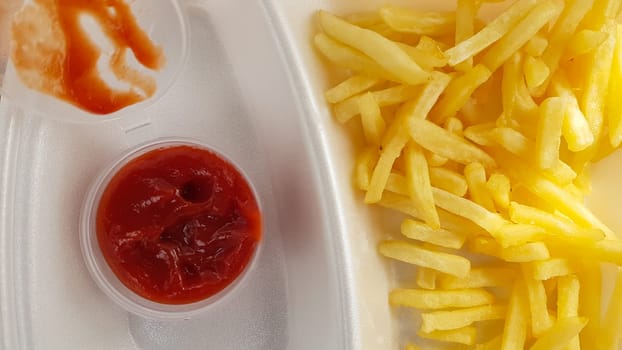 A close-up of golden orange yellow deep fries with tomato ketchup served in a foam container. Fast food takeaway. Unwanted fresh food