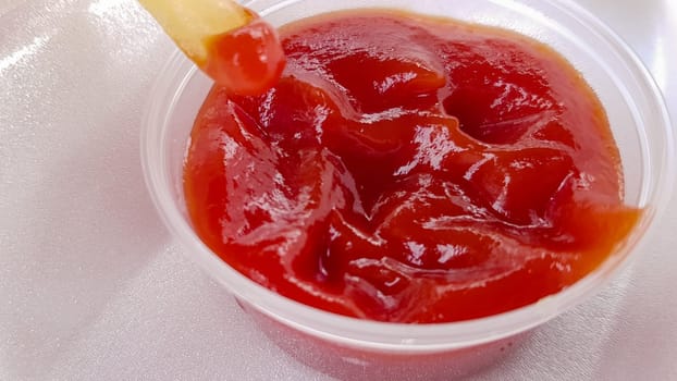 A close-up of golden orange yellow deep fries with tomato ketchup served in a foam container. Fast food takeaway. Unwanted fresh food