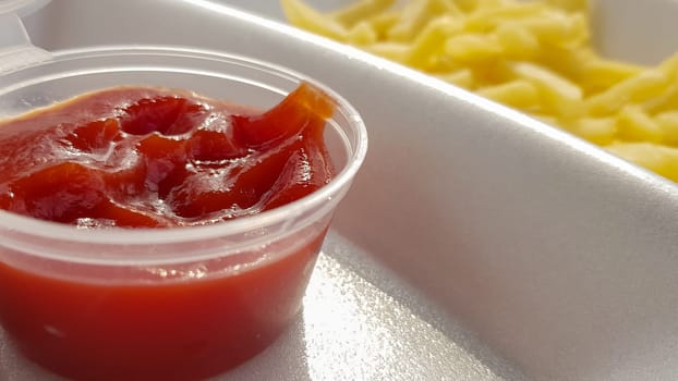 A close-up of golden orange yellow deep fries with tomato ketchup served in a foam container. Fast food takeaway. Unwanted fresh food