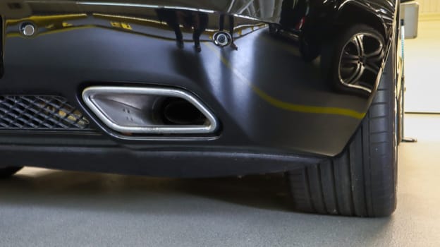 Square tailpipe at the rear right side of a black sports car. Very low plan. The rear bumper, wheel and tailpipe of the packed vehicle are smoke- and gas-free