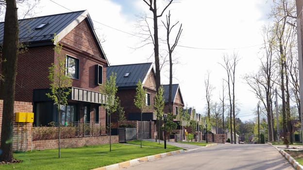 A street with houses and manicured lawns in a typical suburb. Frame made of small brown brick American country houses. Ukraine, Irpin - 07 June 2021