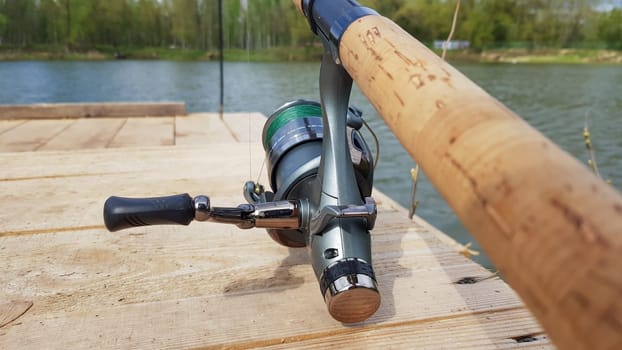 Carp fishing rod isolated on the lake and wooden bridge. Carp feeder spinning reel close up. Fishing for carp on the lake. Fisherman's equipment