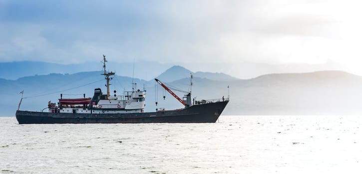 The large fishing vessel on the background of hills and volcanoes
