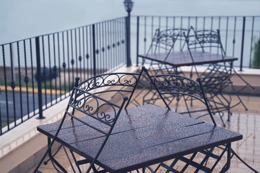 closeup detail of black iron metal chairs near wooden table with rain drops on rainy outdoor restaurant terrace