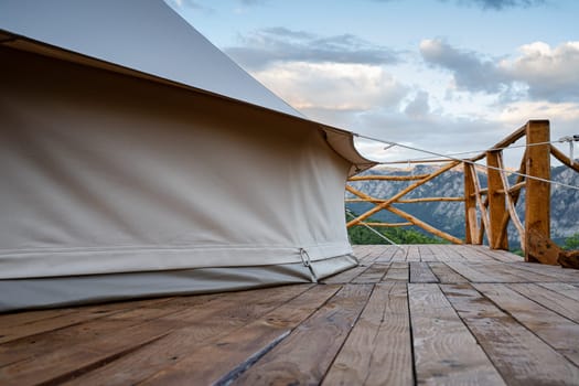 side view closeup of glamping house tent on wooden deck with fence and mountain range scenery in the background