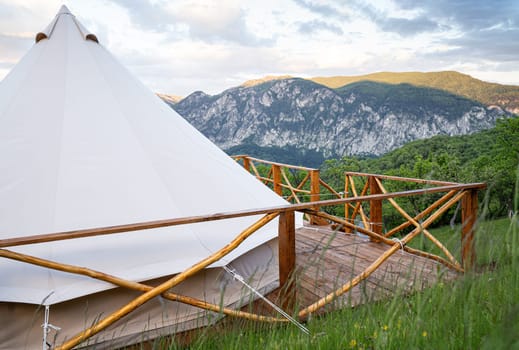 side view closeup of glamping house tent on wooden deck with fence and mountain range scenery in the background