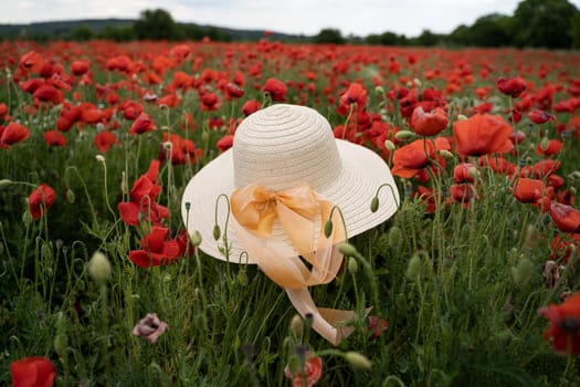 closeup perspective view of woman wicker hat with light colored scarf in field with red poppy flowers