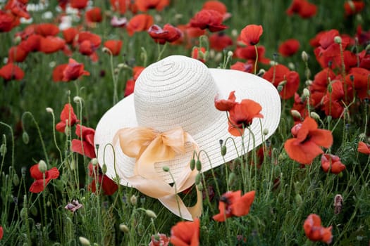 closeup perspective view of woman wicker hat with light colored scarf in field with red poppy flowers