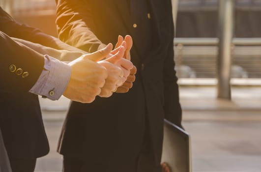 Business people team in black suits standing in city outdoors and showing thumbs up, one of them holding laptop. Teamwork, cooperation and business successful concept