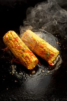 Top view of palatable corn cooking in oil on black surface in kitchen